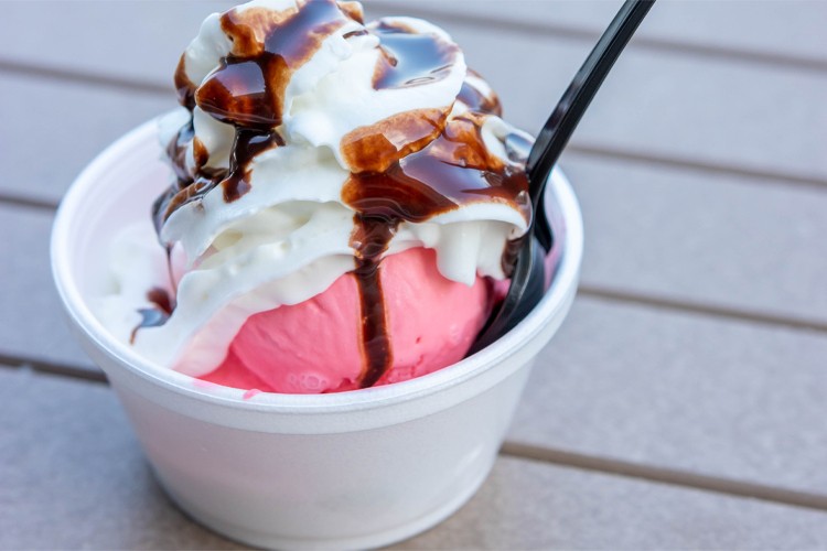 Pink ice cream scoop in a cup with whipped cream and chocolate sauce