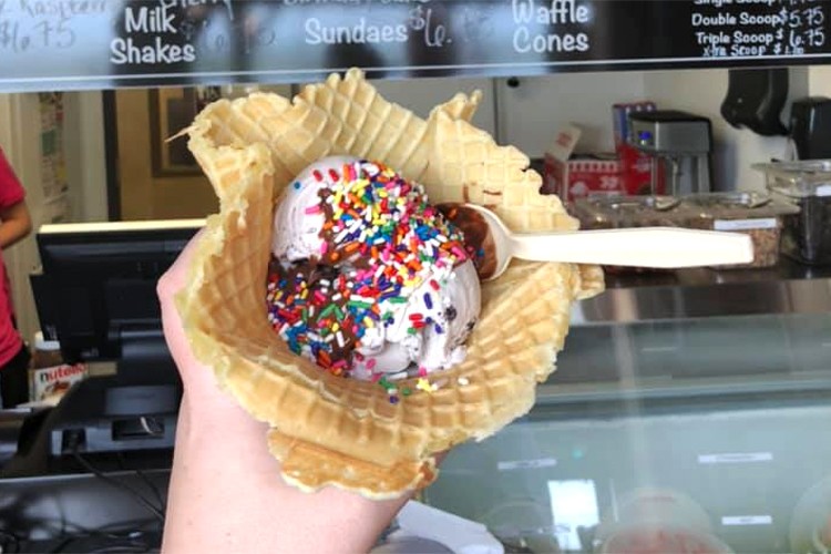 scoops of ice cream in waffle cone bowl with hot fudge and sprinkles